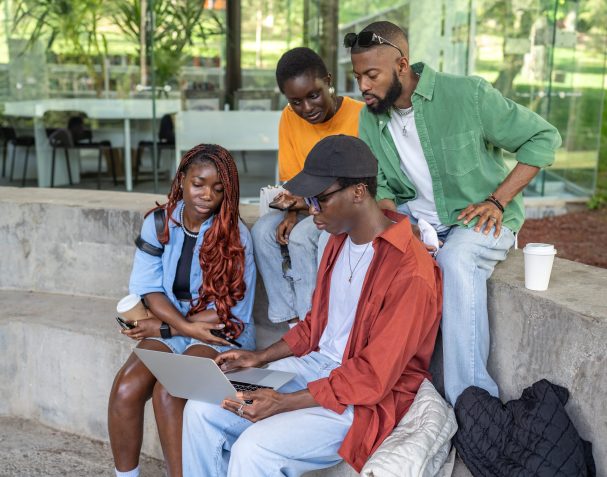 Puzzled African American friends sitting on park bench engaged with laptops. Researching for coursework project, prepare report and online information, university assignments, teamwork outdoors